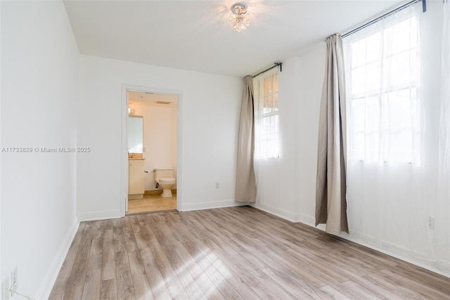 unfurnished bedroom featuring multiple windows, ensuite bath, and light hardwood / wood-style flooring