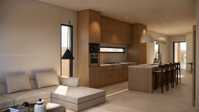 kitchen with an island with sink, black microwave, oven, a kitchen bar, and hanging light fixtures