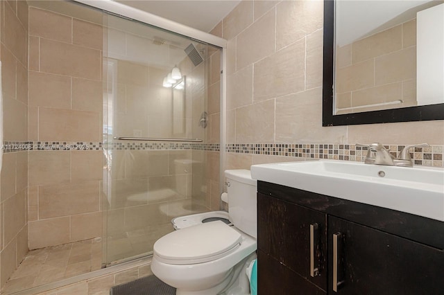 bathroom featuring tile walls, decorative backsplash, vanity, toilet, and a shower with door