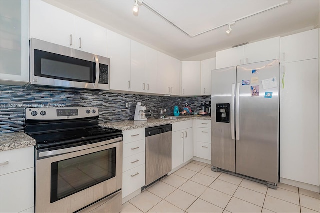 kitchen with white cabinetry, backsplash, stainless steel appliances, light stone countertops, and light tile patterned flooring