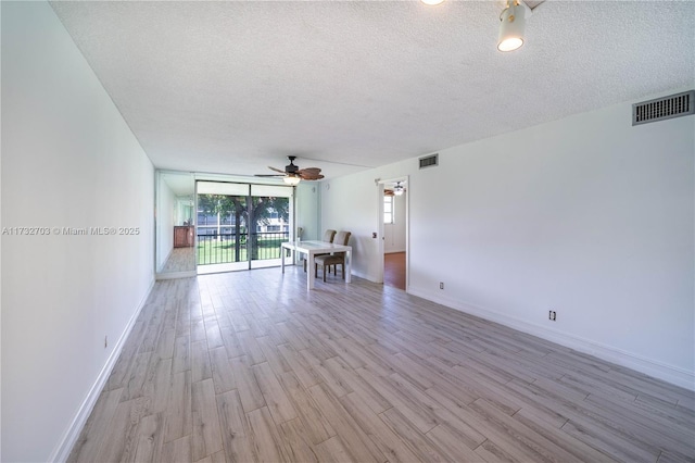 unfurnished room featuring expansive windows, ceiling fan, light hardwood / wood-style flooring, and a textured ceiling