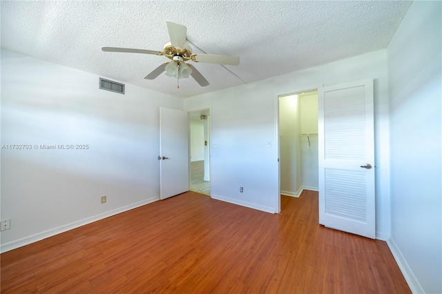 unfurnished bedroom featuring ceiling fan, wood-type flooring, a textured ceiling, a walk in closet, and a closet