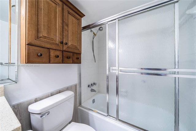 bathroom featuring toilet and bath / shower combo with glass door