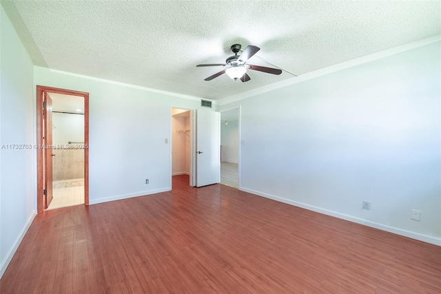 unfurnished bedroom featuring ensuite bath, a walk in closet, a closet, ceiling fan, and hardwood / wood-style floors