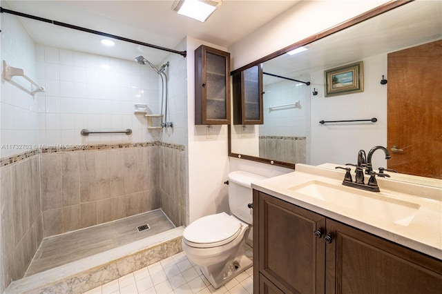 bathroom with tile patterned flooring, vanity, tiled shower, and toilet