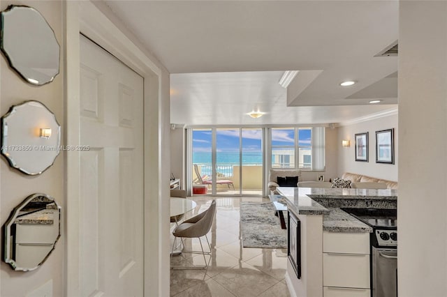 kitchen featuring stone countertops, white cabinets, expansive windows, ornamental molding, and a water view