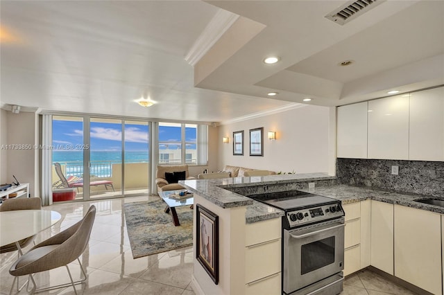 kitchen with a water view, dark stone countertops, a tray ceiling, kitchen peninsula, and electric stove