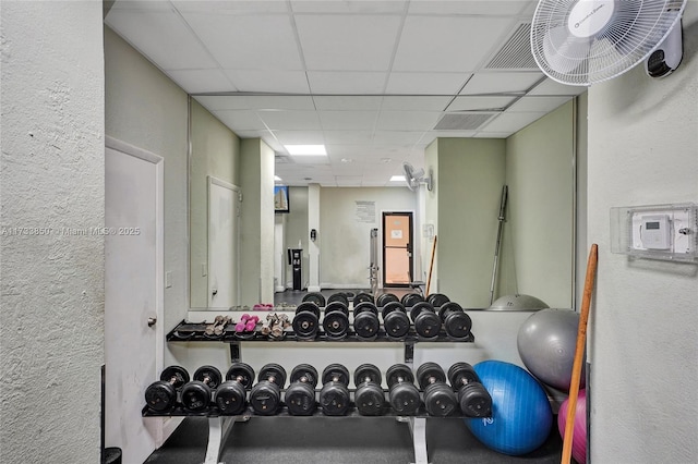 exercise area featuring a textured wall and a drop ceiling