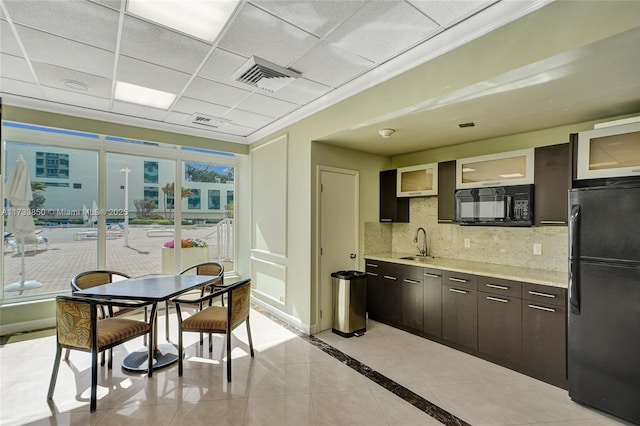 kitchen featuring visible vents, dark brown cabinetry, light countertops, a sink, and black appliances