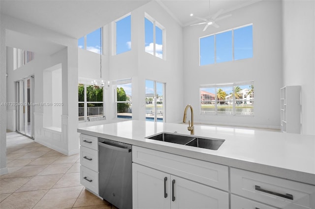 kitchen featuring light tile patterned flooring, sink, stainless steel dishwasher, a towering ceiling, and white cabinets