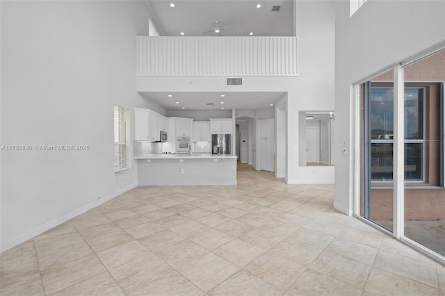 unfurnished living room featuring a towering ceiling, light tile patterned floors, and ceiling fan