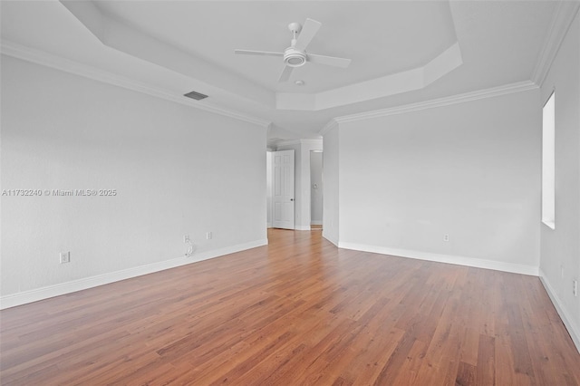 empty room with ceiling fan, ornamental molding, a raised ceiling, and light wood-type flooring