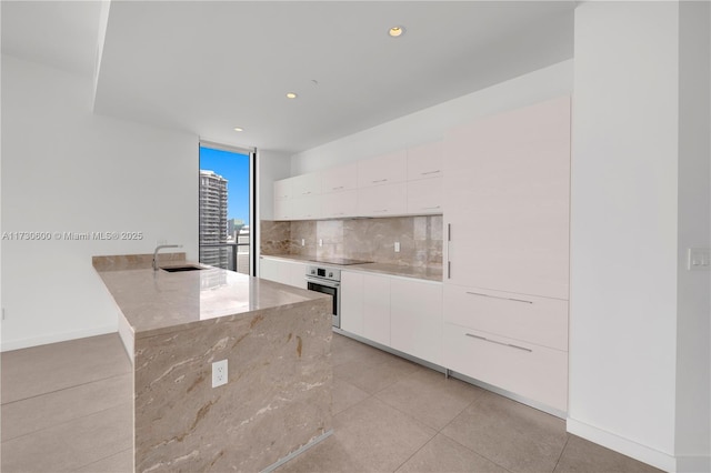 interior space with sink, white cabinetry, stainless steel oven, black electric cooktop, and decorative backsplash