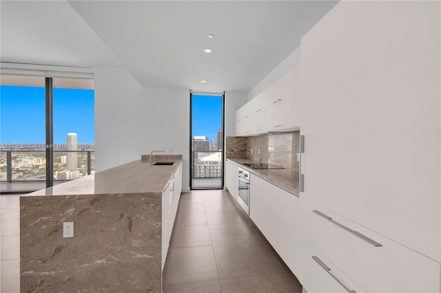 kitchen featuring floor to ceiling windows, sink, white cabinetry, black electric cooktop, and dark stone counters