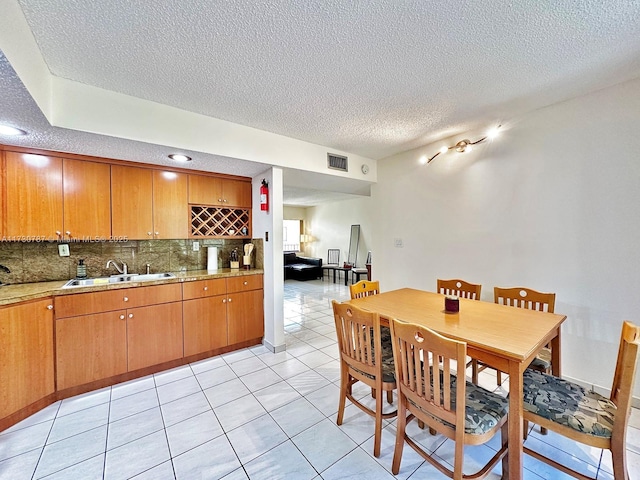 kitchen featuring sink, decorative backsplash, a textured ceiling, and light tile patterned flooring