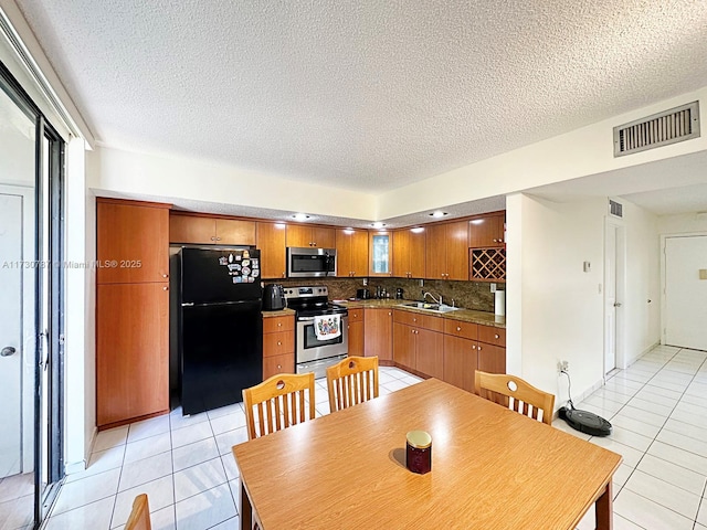 kitchen with light tile patterned flooring, appliances with stainless steel finishes, sink, backsplash, and a textured ceiling