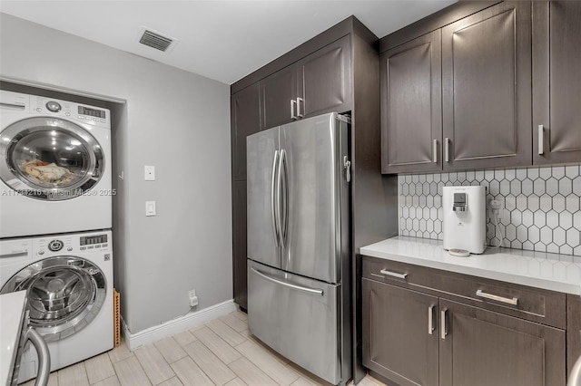 kitchen featuring stainless steel refrigerator, dark brown cabinets, stacked washer and clothes dryer, and tasteful backsplash