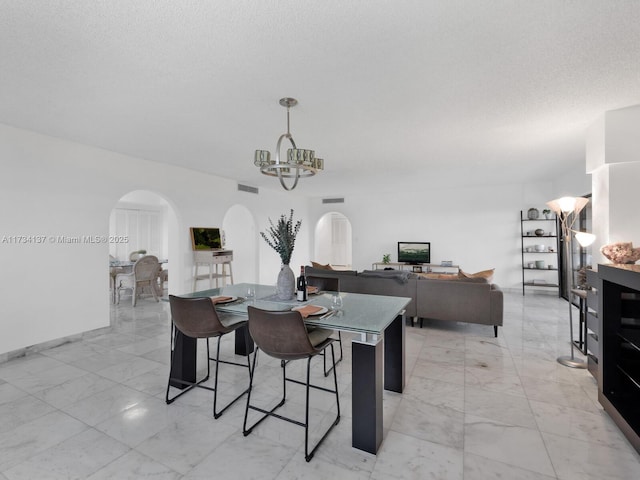 dining space featuring visible vents, arched walkways, a notable chandelier, marble finish floor, and a textured ceiling