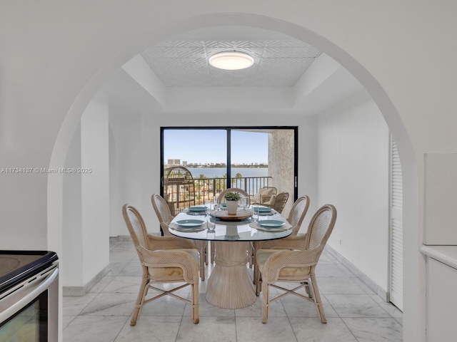 dining space with baseboards, a raised ceiling, and marble finish floor