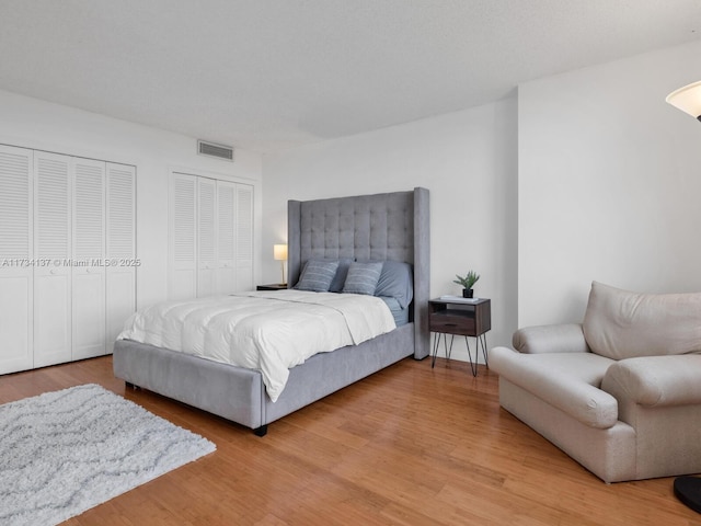 bedroom featuring two closets, visible vents, and light wood finished floors