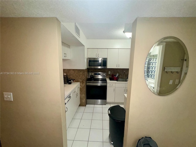 kitchen with light tile patterned floors, appliances with stainless steel finishes, a textured ceiling, white cabinets, and decorative backsplash