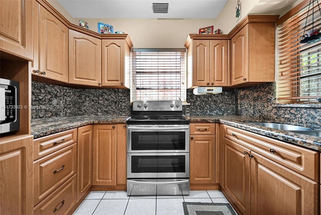 kitchen featuring sink, dark stone countertops, light tile patterned floors, stainless steel appliances, and decorative backsplash