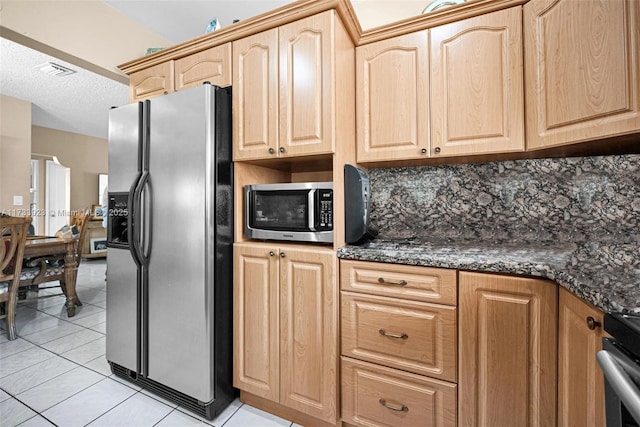 kitchen featuring dark stone countertops, backsplash, light tile patterned floors, stainless steel appliances, and light brown cabinets