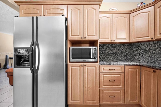 kitchen featuring light brown cabinetry, tasteful backsplash, dark stone countertops, light tile patterned floors, and stainless steel appliances