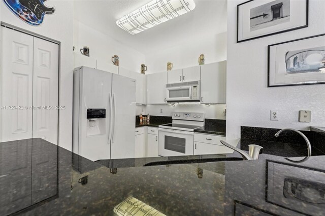 kitchen with white cabinetry, white appliances, and dark stone counters