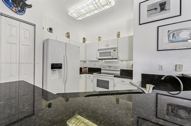 kitchen with white appliances, dark stone counters, and white cabinets