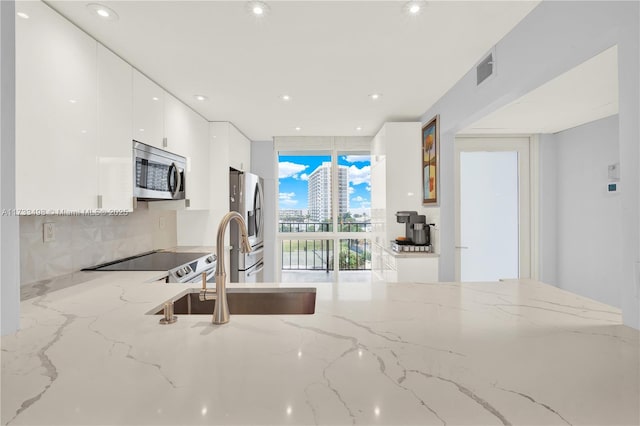 kitchen with floor to ceiling windows, tasteful backsplash, stainless steel appliances, light stone countertops, and white cabinets