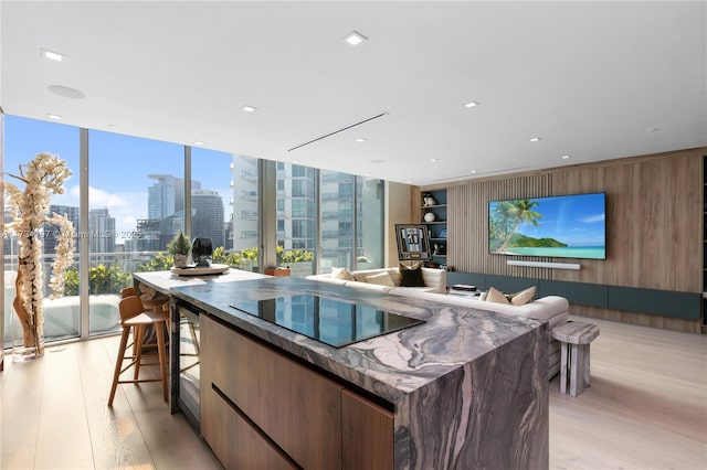 kitchen featuring a breakfast bar area, wooden walls, black electric stovetop, light hardwood / wood-style floors, and expansive windows