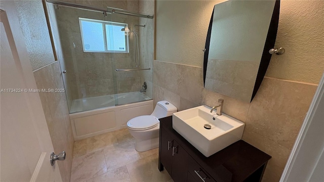 full bathroom with tile walls, vanity, shower / bath combination with glass door, and toilet