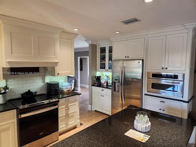 kitchen featuring appliances with stainless steel finishes, dark stone countertops, white cabinets, backsplash, and light tile patterned floors