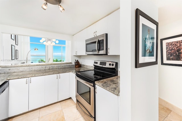 kitchen with stainless steel appliances, white cabinetry, light tile patterned floors, and dark stone counters