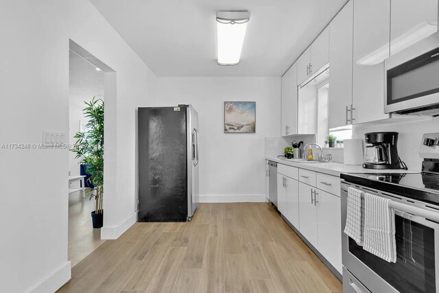 kitchen with light wood-type flooring, appliances with stainless steel finishes, sink, and white cabinets