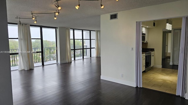 empty room featuring dark wood-type flooring, a wall of windows, and a textured ceiling