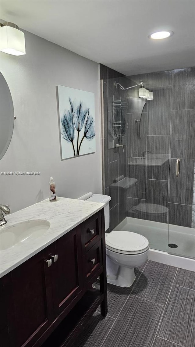 bathroom featuring a shower with door, vanity, and toilet