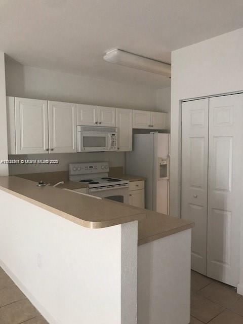 kitchen with white appliances, tile patterned floors, white cabinets, and kitchen peninsula