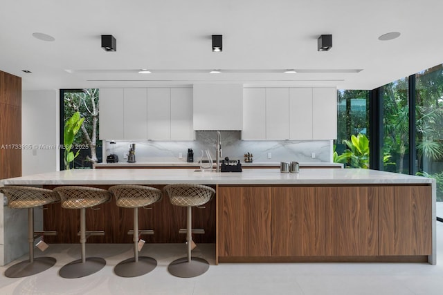 kitchen featuring floor to ceiling windows, sink, white cabinetry, a large island, and decorative backsplash