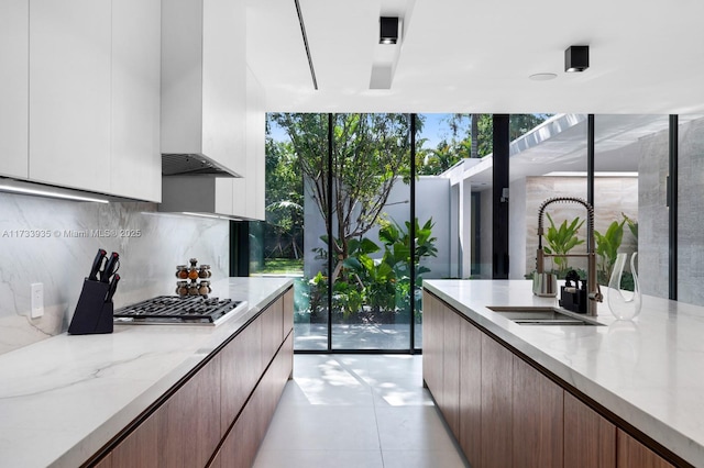 4040 Kiaora St, Miami, FL 33133 - kitchen featuring stainless steel gas cooktop, modern cabinets, wall chimney range hood, tasteful backsplash, and light stone counters