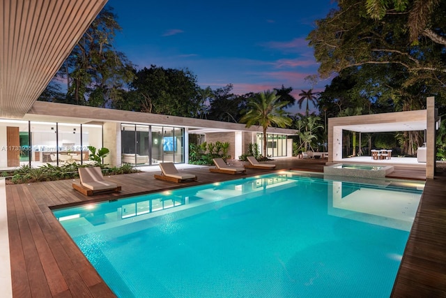 pool at dusk featuring a wooden deck and an in ground hot tub