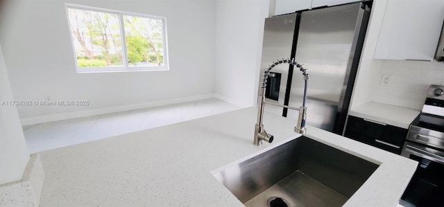 interior details with appliances with stainless steel finishes, white cabinets, light stone counters, and decorative backsplash