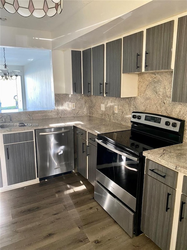 kitchen with appliances with stainless steel finishes, an inviting chandelier, backsplash, dark hardwood / wood-style floors, and light stone counters