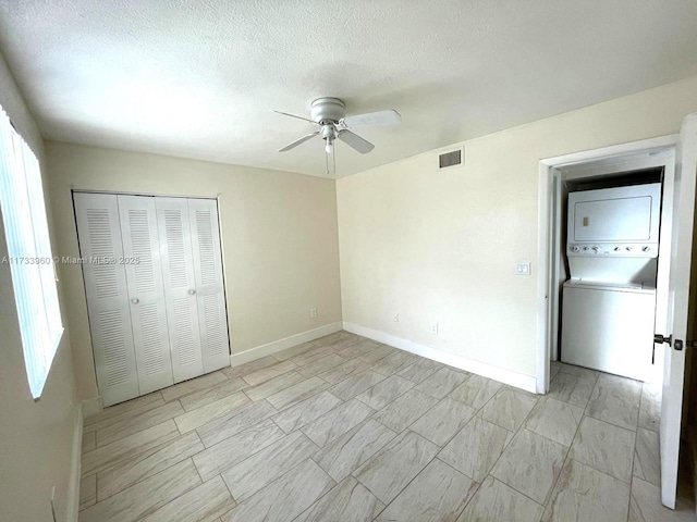 unfurnished bedroom featuring ceiling fan, stacked washer and clothes dryer, a closet, and a textured ceiling