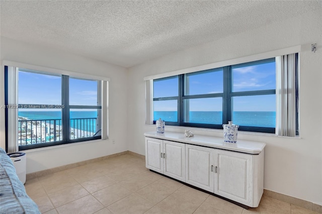 interior space with a water view, light tile patterned floors, white cabinets, and a textured ceiling