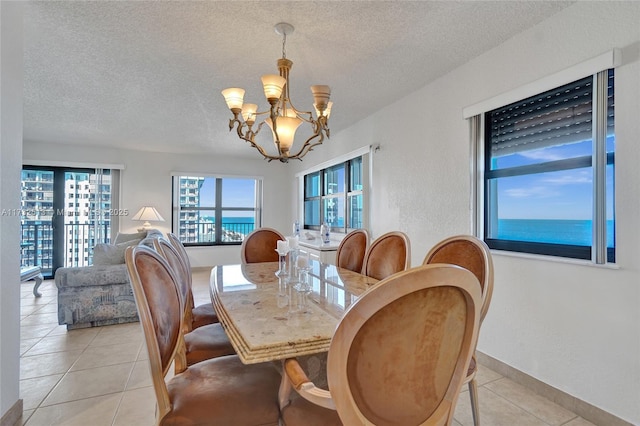 dining space featuring a notable chandelier, light tile patterned flooring, a textured ceiling, and a water view