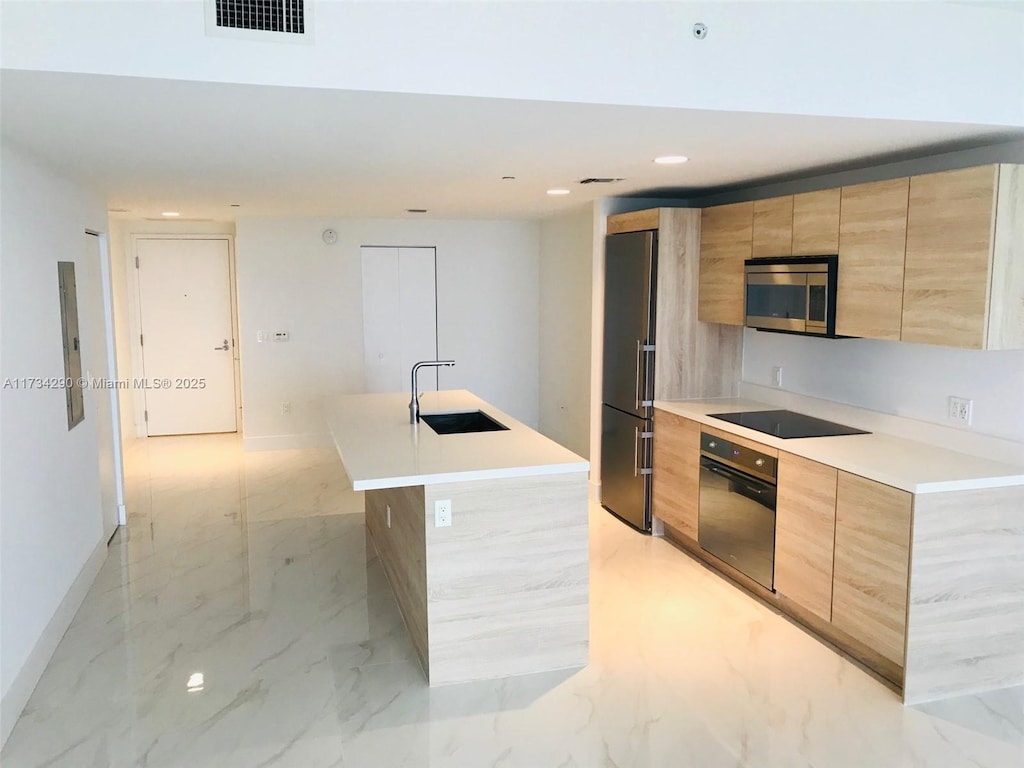 kitchen featuring an island with sink, appliances with stainless steel finishes, sink, and light brown cabinetry