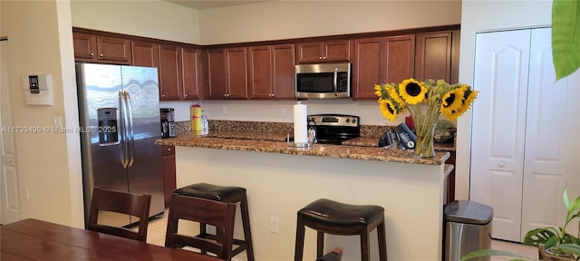 kitchen featuring a kitchen breakfast bar, stainless steel appliances, dark stone counters, and kitchen peninsula