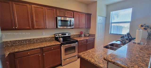 kitchen with dark stone countertops, sink, light tile patterned floors, and appliances with stainless steel finishes